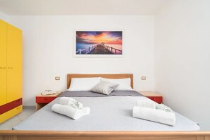 Un dormitorio con una cama de madera, una mesita de noche, un armario amarillo y un cuadro de atardecer en la pared.