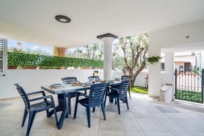 An outdoor dining area with a table and chairs, a pergola, and a view of the surrounding greenery and buildings. - Cala Luna - Two Bedroom Apartment, Sleeps 7 (Orosei)