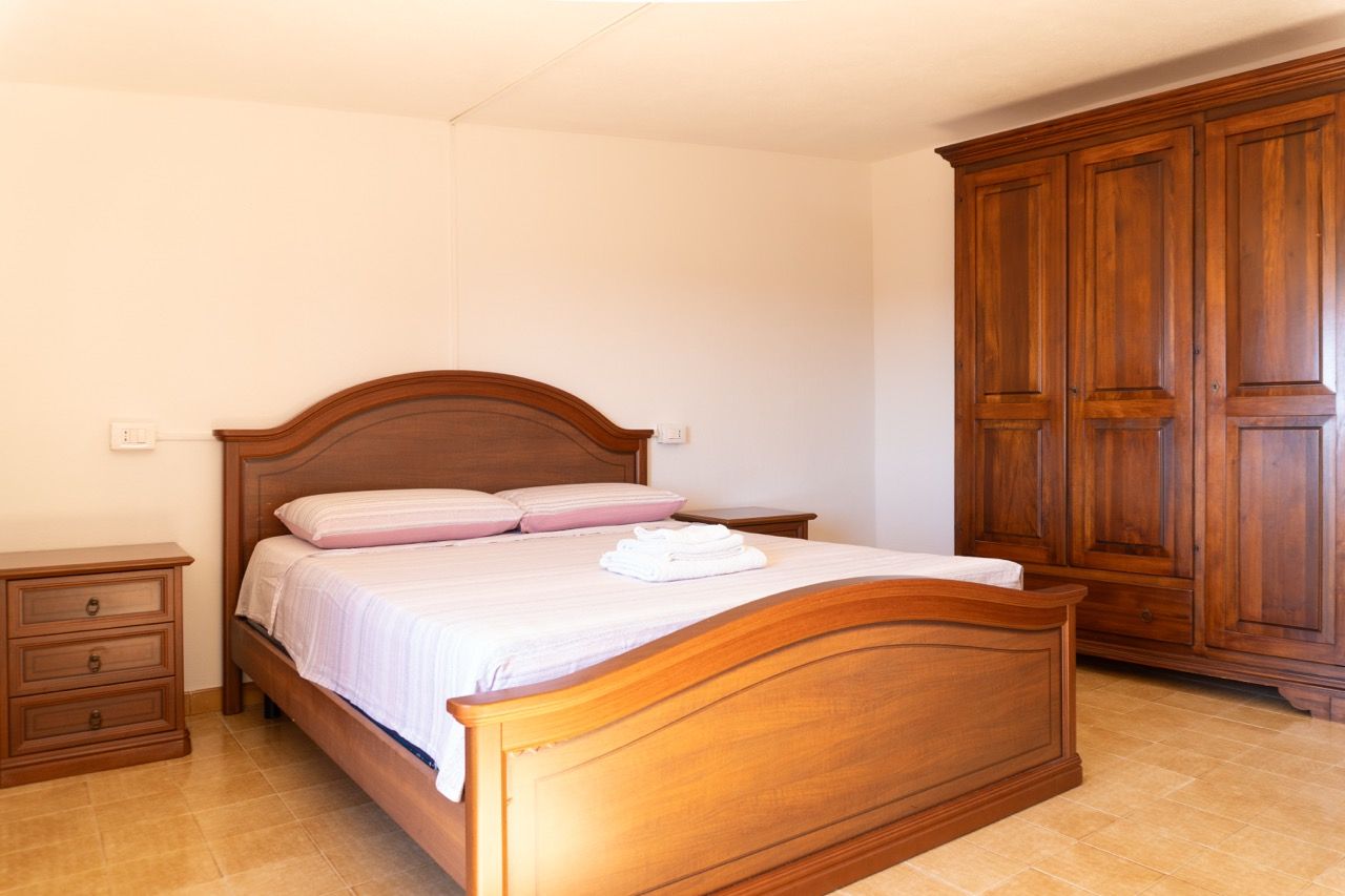 A bedroom with a wooden bed, a nightstand, a wardrobe, and a tiled floor.