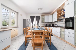 Een moderne keuken met witte kasten, een eettafel gedekt voor vier personen en uitzicht op de omgeving door grote ramen.