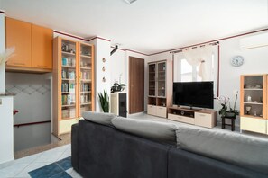 Een moderne woonkamer met een bank, televisie, open kasten en een boekenkast.