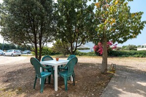 An outdoor seating area with a table and chairs, surrounded by trees and a view of a body of water. - Su Nidu Virde - Four Bedroom House, Sleeps 9 (Orosei)
