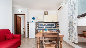Ett kompakt bostadsutrymme med en matplats, ett litet kök och en röd soffa.