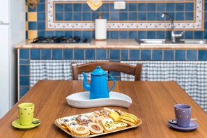 Keittiö, jossa on ruutukuosinen pöytäliina, tarjotin, jossa on erilaisia leivonnaisia, sininen teekannu ja kaksi kuppia.
