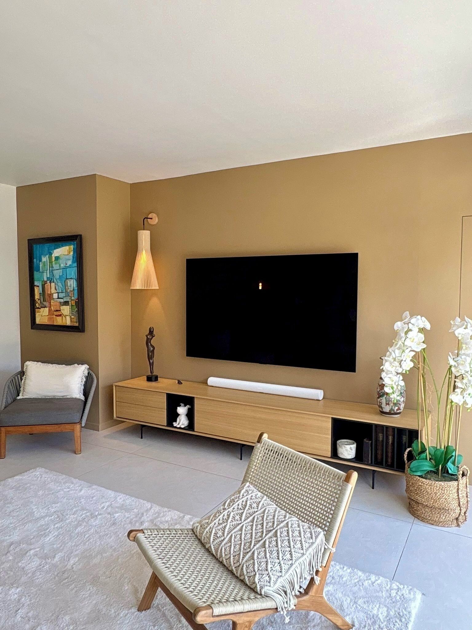 A modern living room with a flat-screen TV, a sofa, a chair, a lamp, and decorative items.