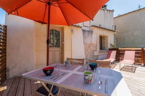 An outdoor dining area with a table set for two, a red umbrella, and a view of a building with a tiled roof. - “Domaine De Meyrol - Gîte 4” Apartment with Mountain View, Wi-Fi, and Air Conditioning (Eyguières)