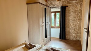 Ein Zimmer mit Schrank, Bett mit Handtüchern, einer Steinwand und einem Fenster mit Vorhängen.