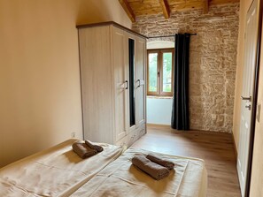 Ein Zimmer mit Schrank, Bett mit Handtüchern, einer Steinwand und einem Fenster mit Vorhängen.