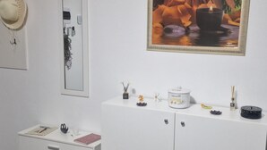 Un mur blanc orné d’un tableau encadré, une armoire blanche agrémentée d’objets décoratifs, une porte blanche et une commode blanche avec des tiroirs.