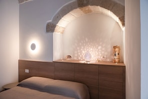 A bedroom with a bed, a nightstand, a wall-mounted light, and a decorative item. - Pachita's Seaside Rooms - Polignano a Mare (Polignano a Mare)