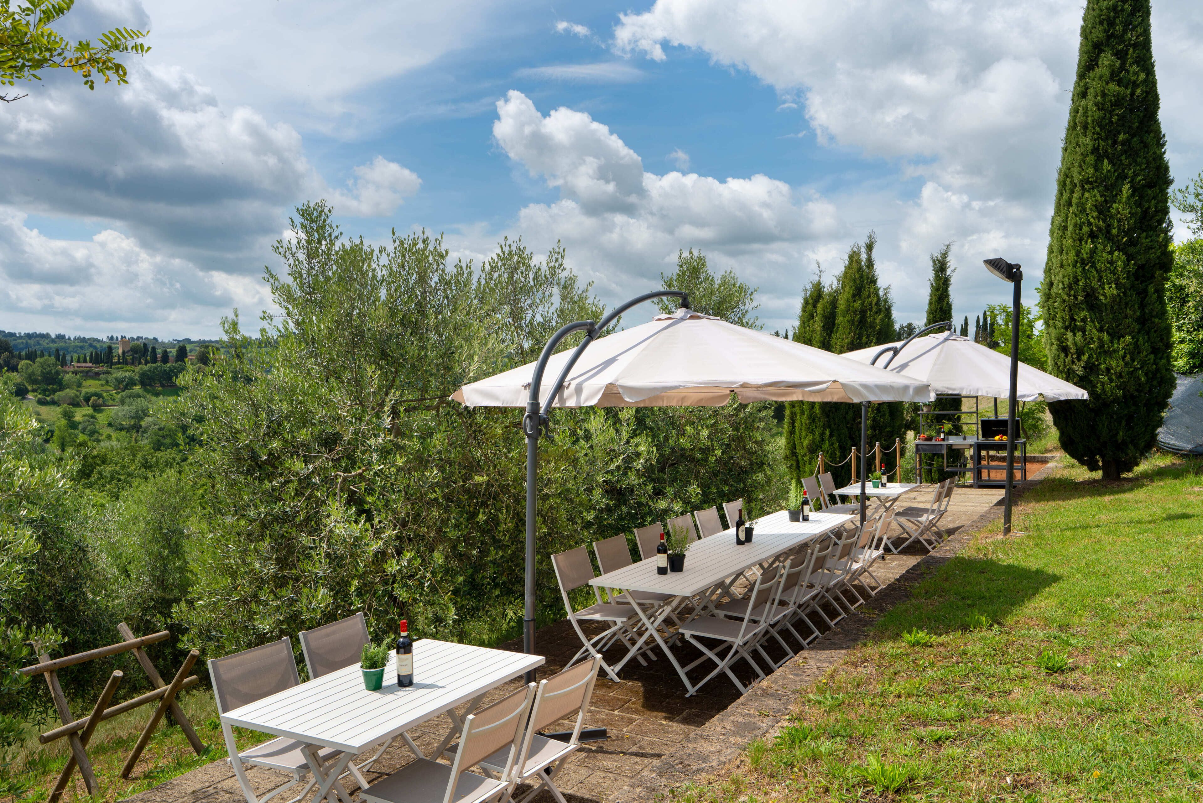 An outdoor dining area with white tables and chairs, umbrellas, and a view of the countryside.