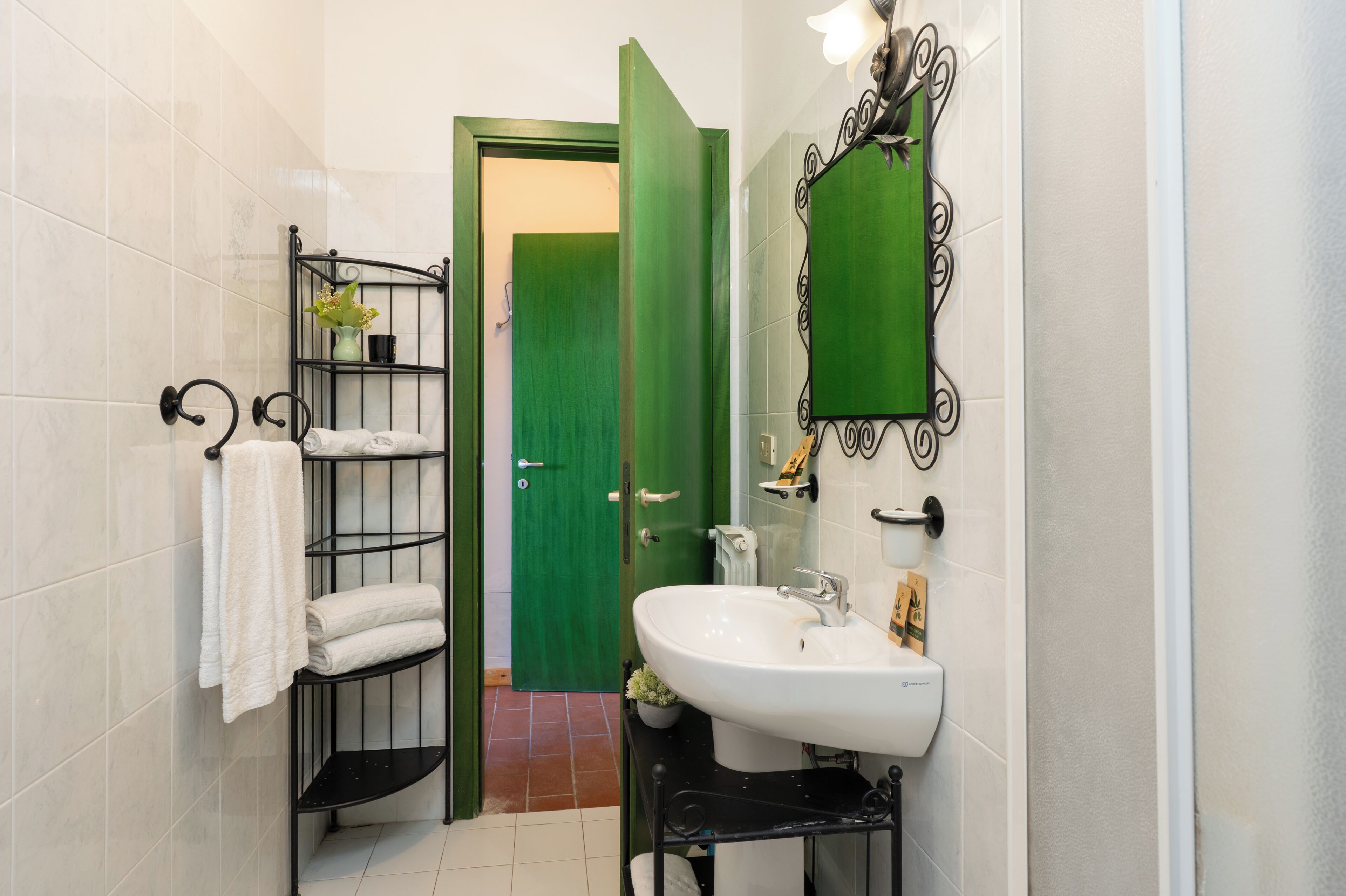 Une salle de bain avec une porte verte, un lavabo blanc et une étagère en métal noir sur laquelle sont posées des serviettes.