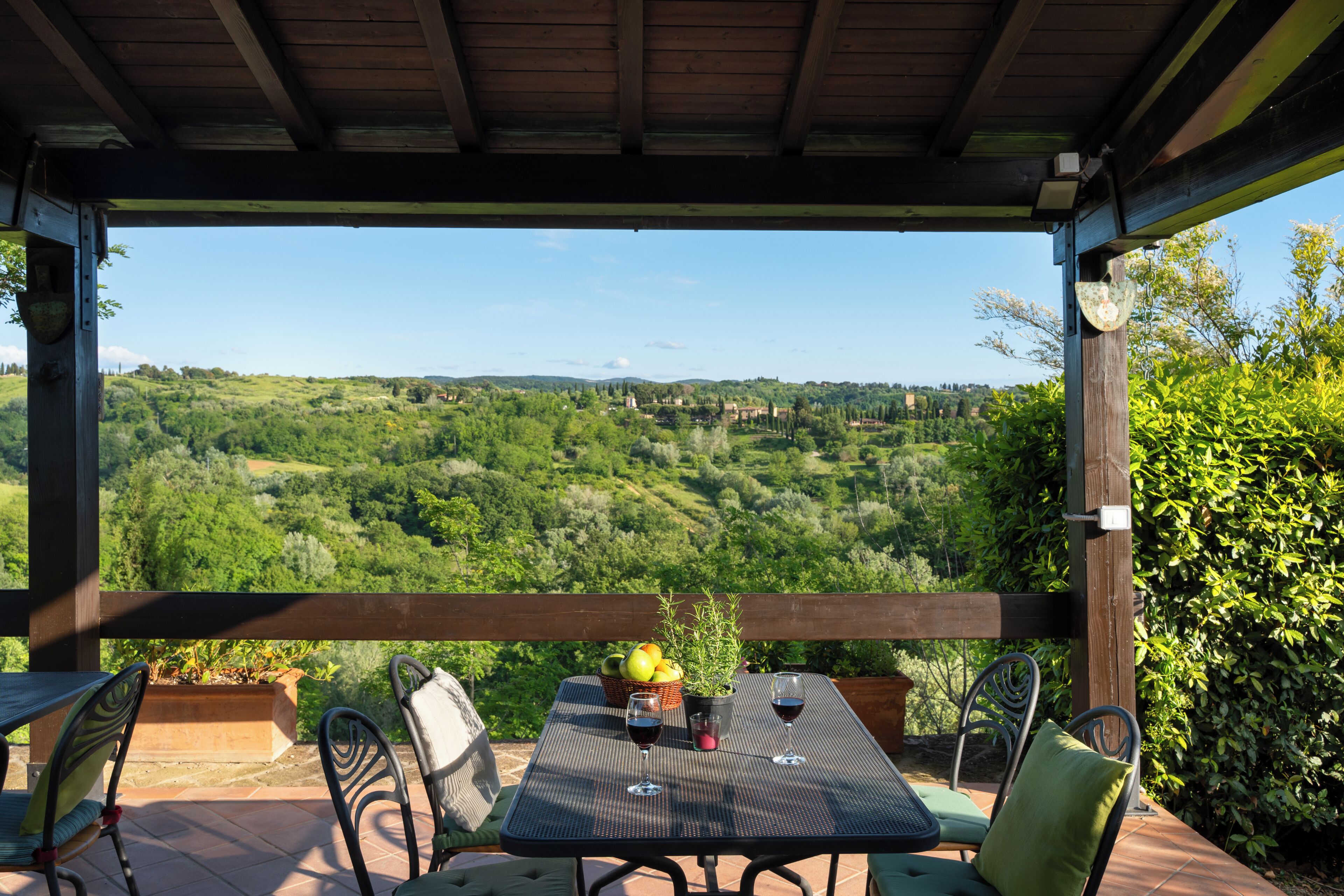 Ein überdachter Außenbereich mit Tisch, Stühlen und Blick auf eine grüne Landschaft.