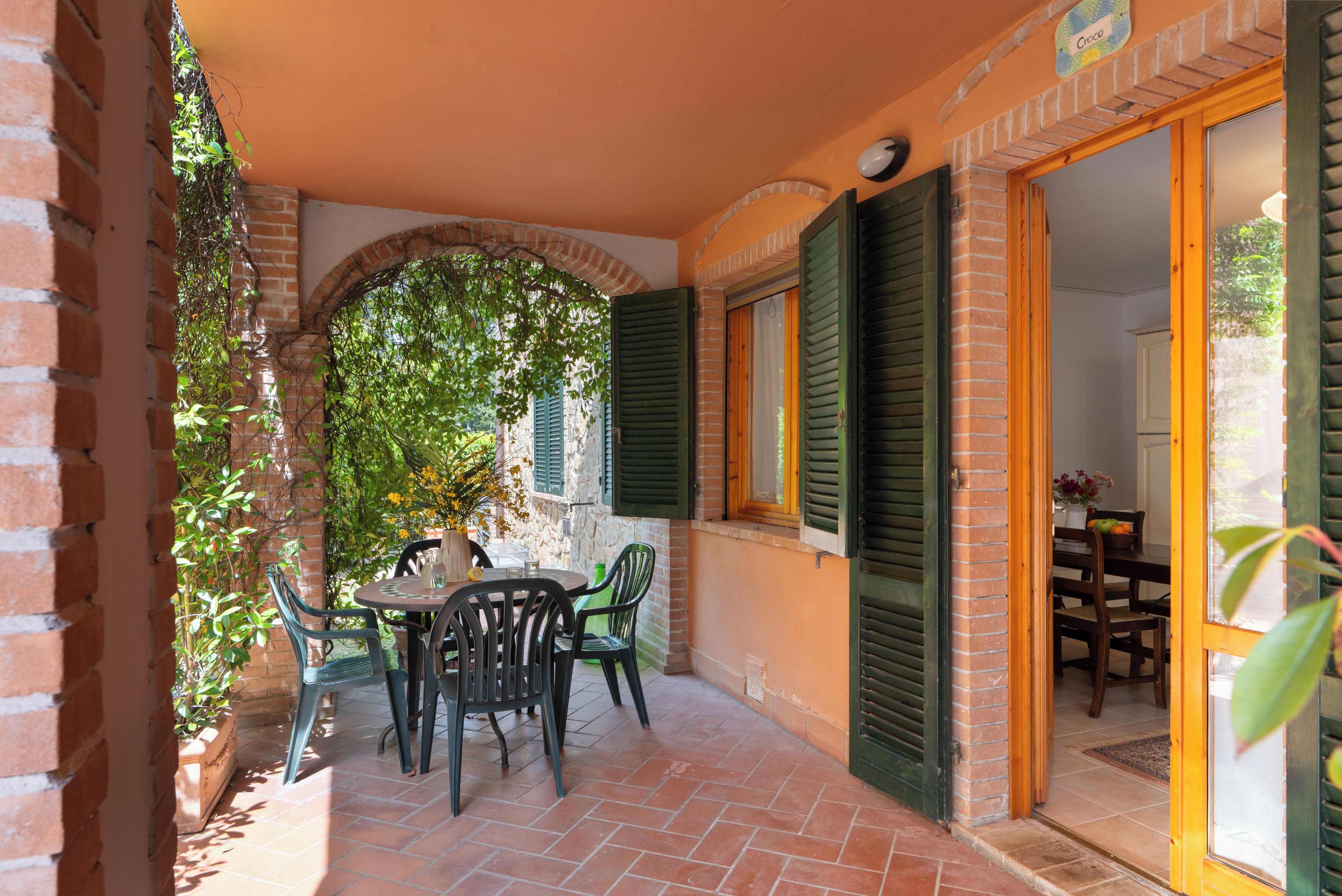 Un patio con una mesa, sillas, un muro de ladrillo y una puerta que da a un espacio interior.