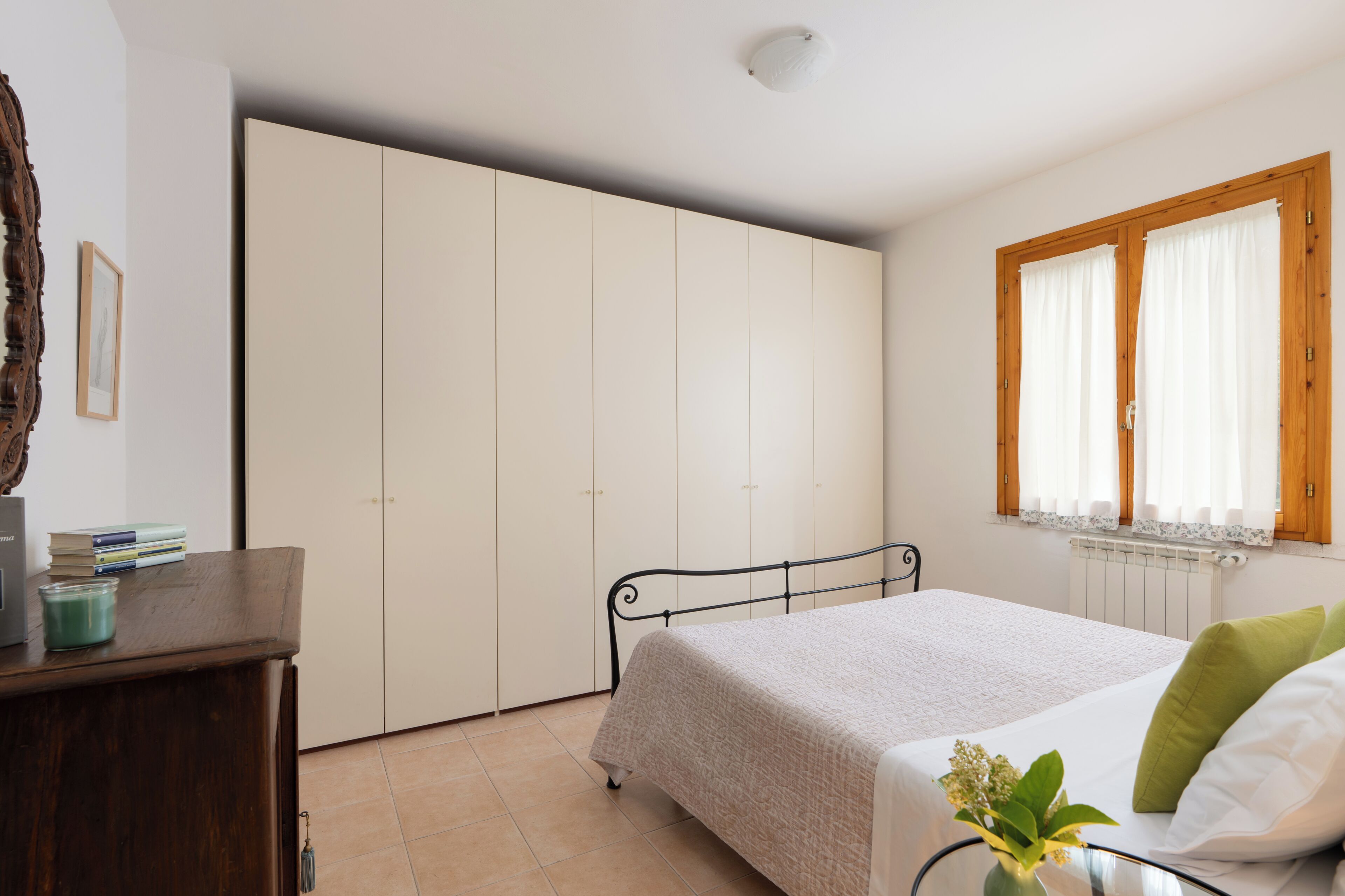 A bedroom with a bed, a wardrobe, a window with curtains, and a bedside table with a vase.