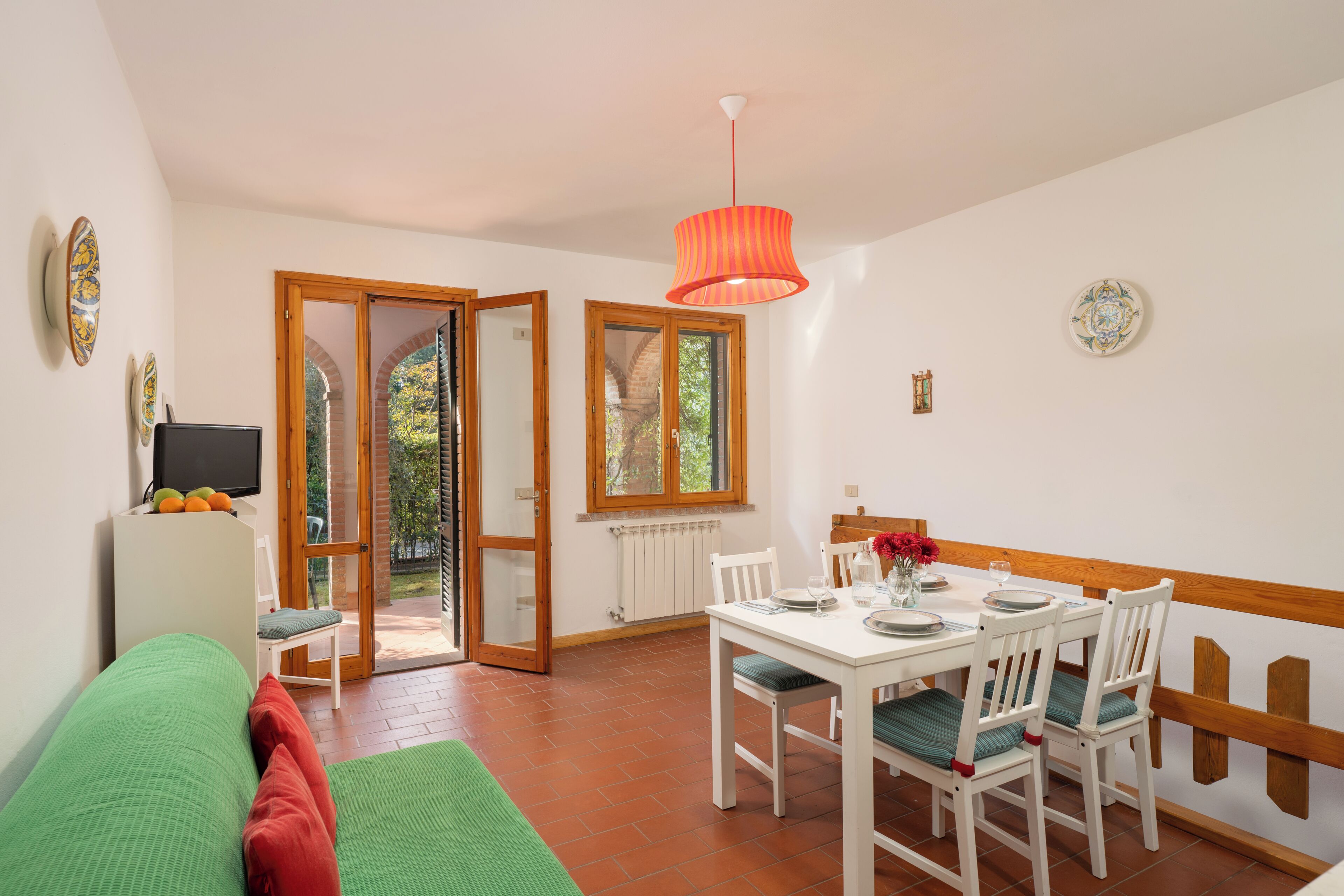 A room with a dining table, chairs, a sofa, a television, and a door leading to an outdoor area.