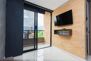 A modern room with a large sliding glass door, a flat-screen TV mounted on a brick wall, and a small shelf with a bicycle and a sign. - Hotel Distrito 70 Living  (Medellín)