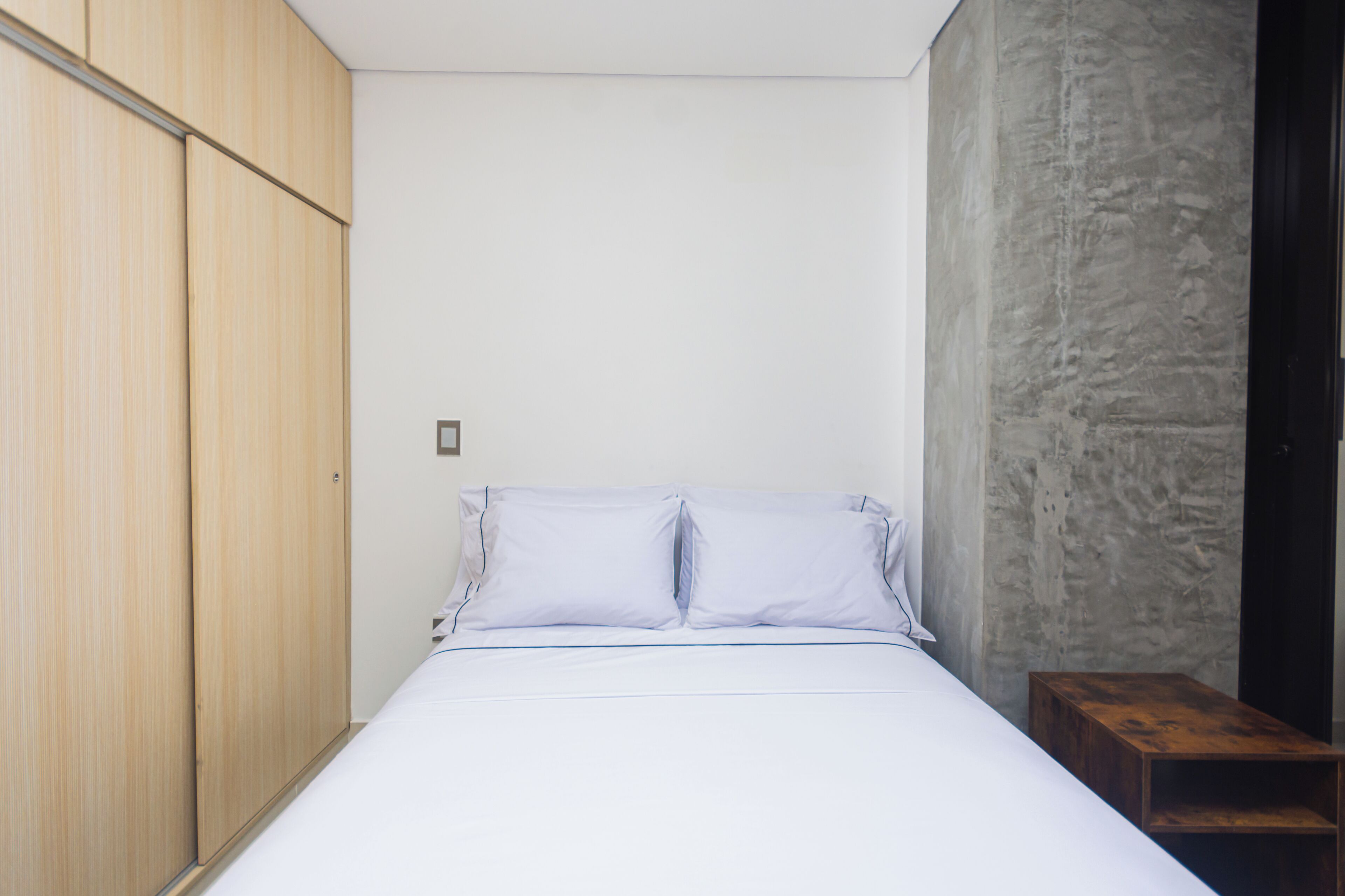 A bedroom with a bed, wooden wardrobe, and a concrete wall.