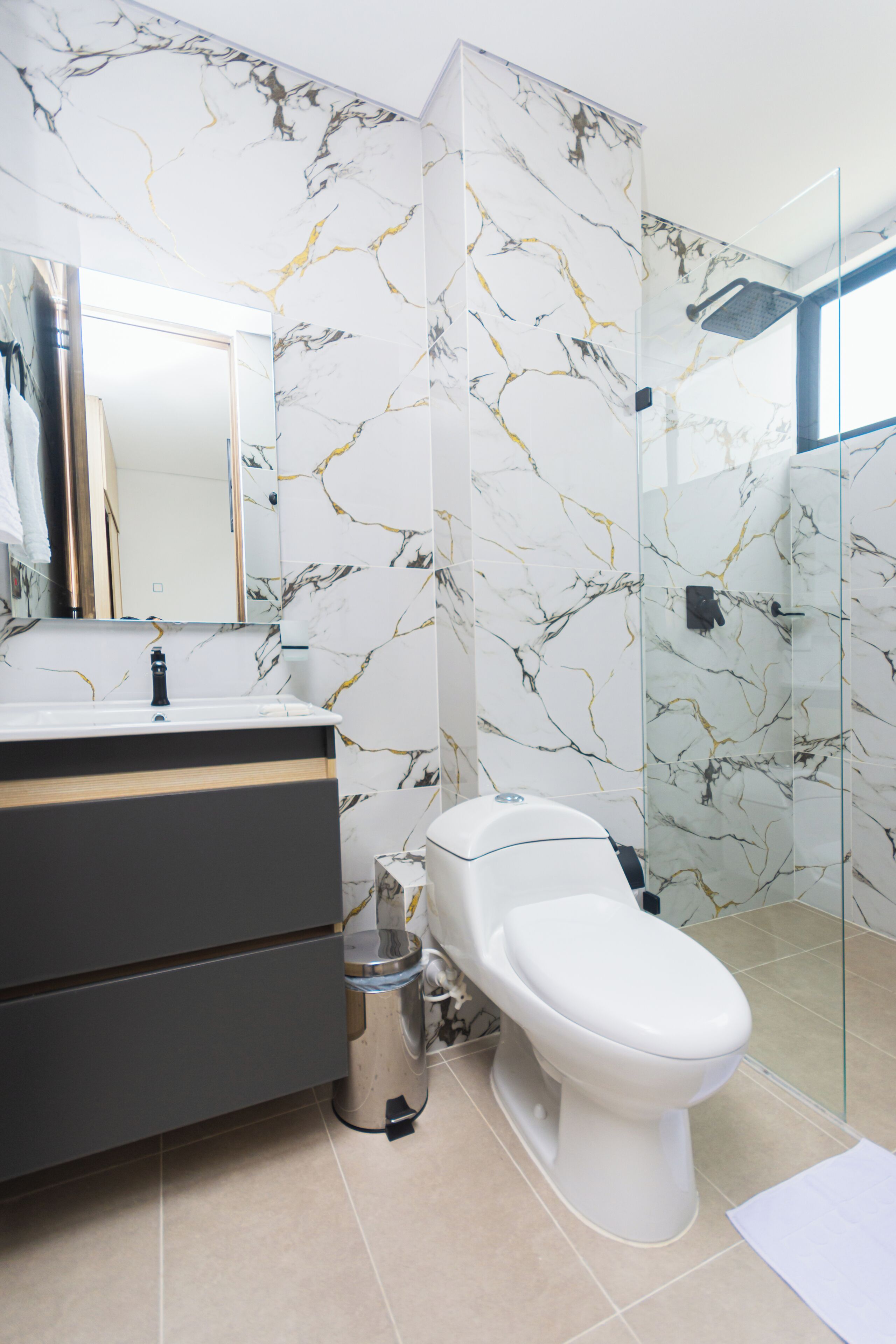 A bathroom with a marble backsplash, a modern sink, a toilet, and a glass shower enclosure.