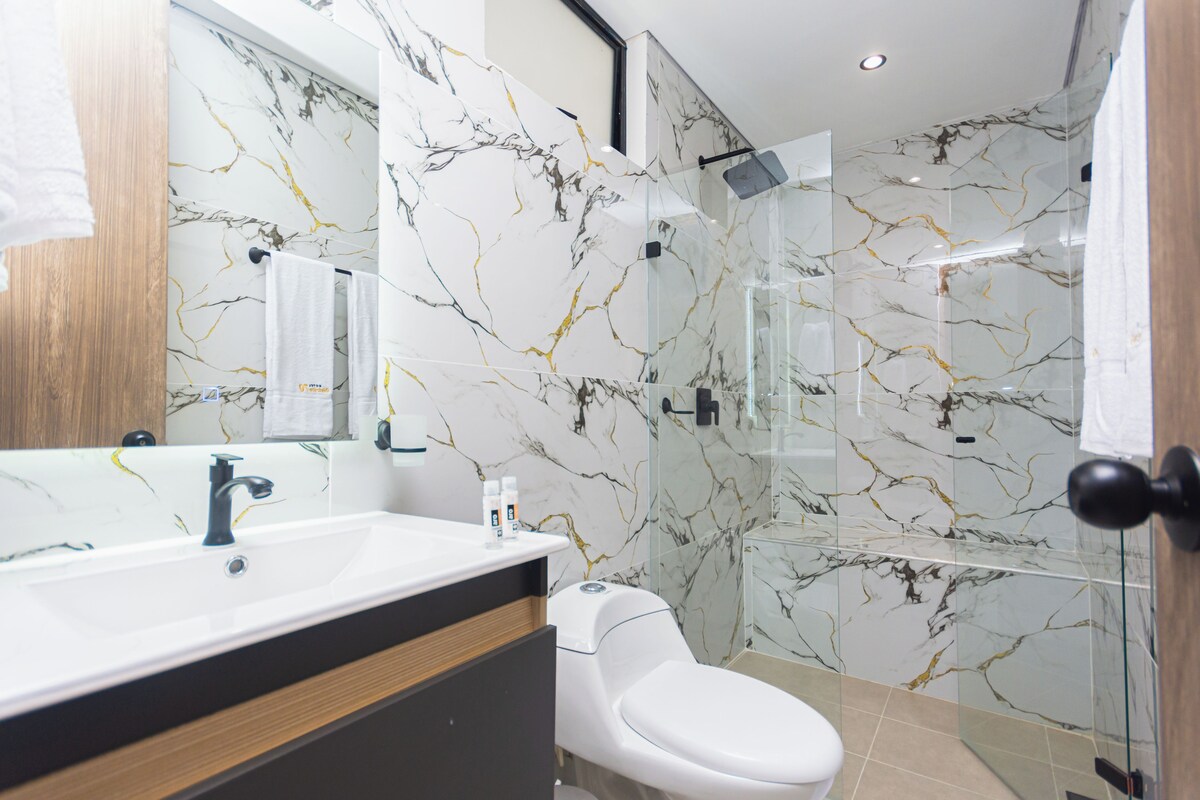 Un baño moderno con salpicadero de mármol, un lavabo blanco y una cabina de ducha de vidrio.