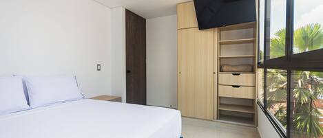 A bedroom with a bed, a wardrobe, and a window with a view of palm trees.