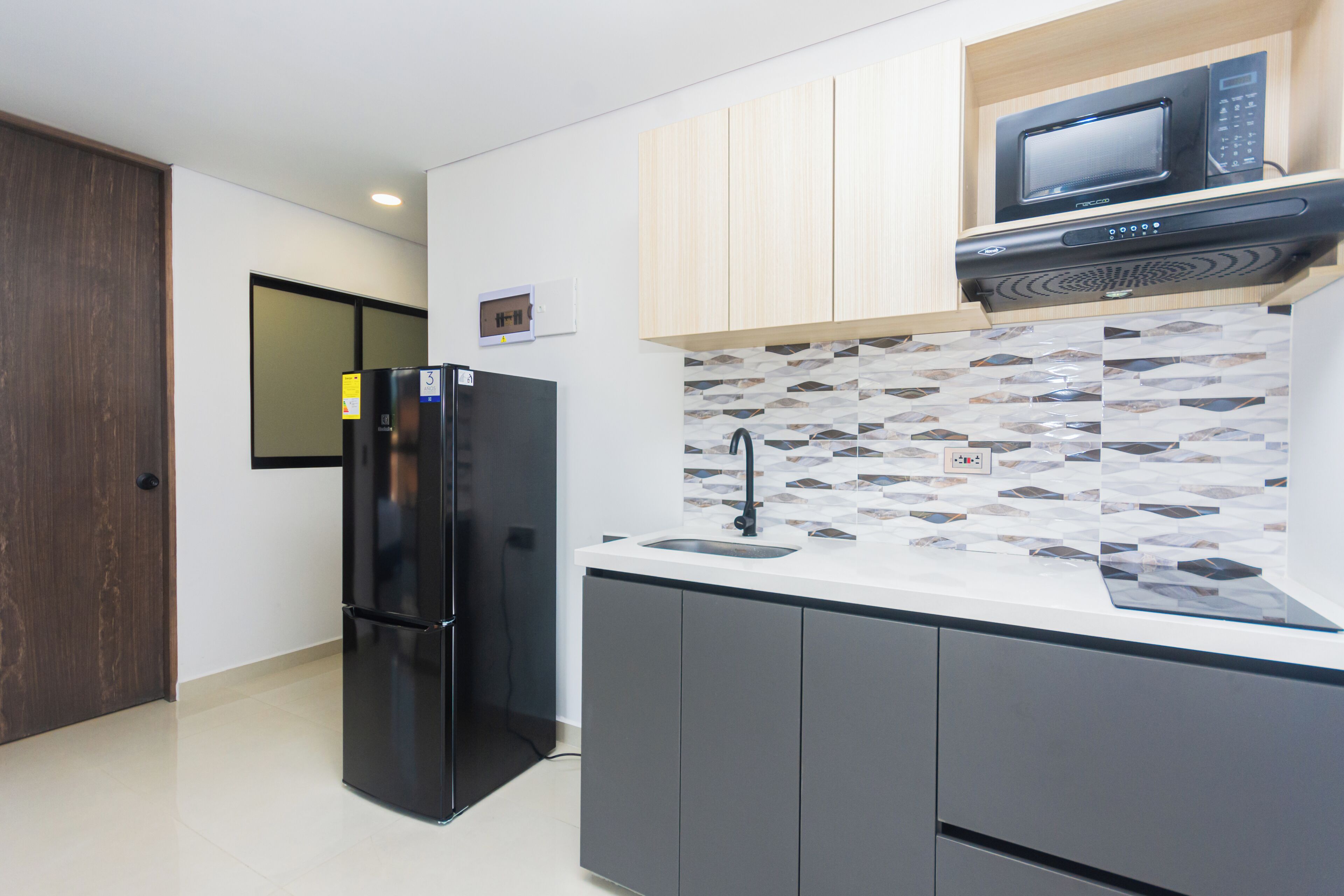 A modern kitchen with a black refrigerator, a microwave, and a tiled backsplash.