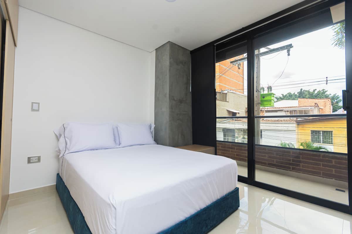 Un dormitorio con cama, ventana y vista a edificios.