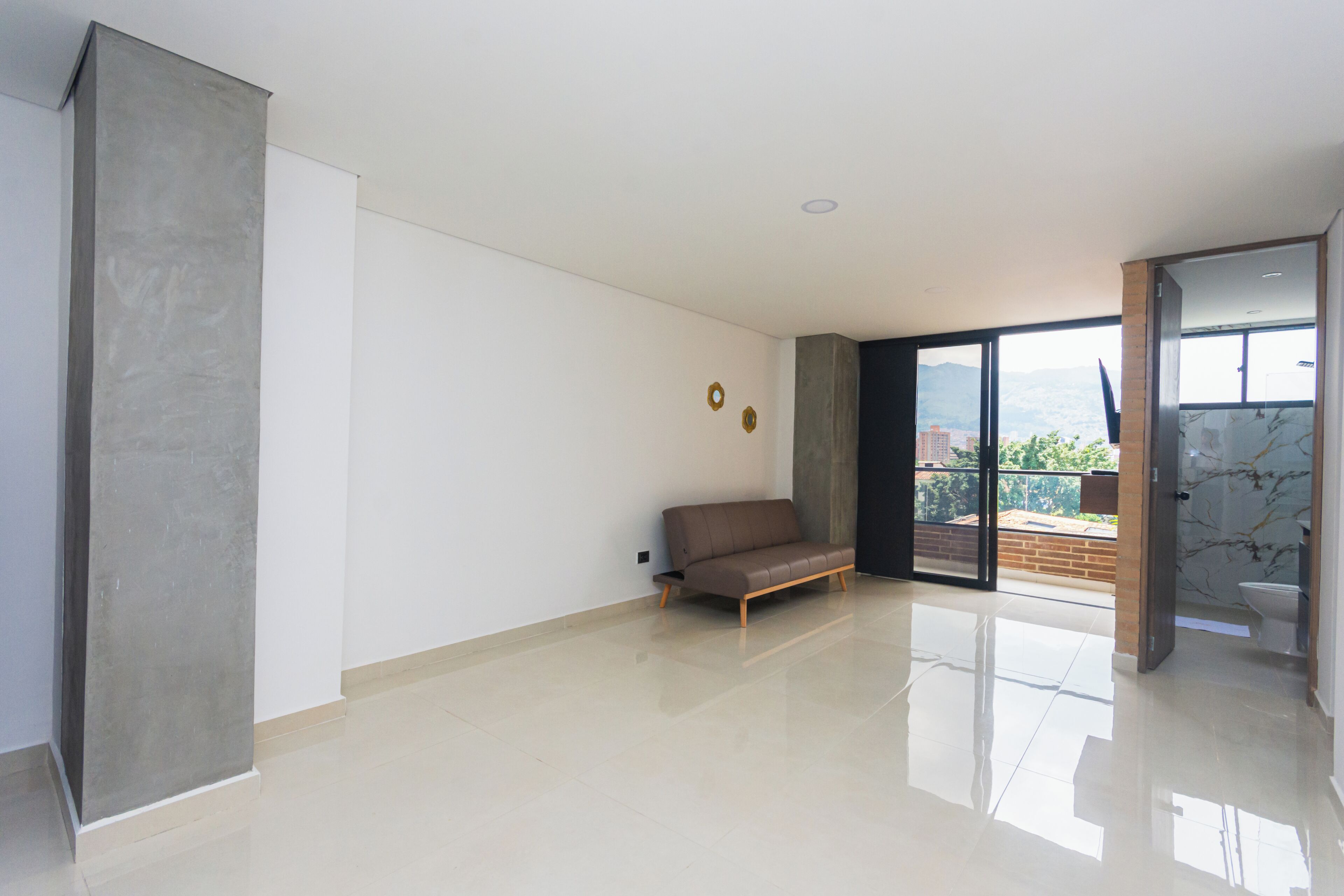 Ruime kamer met een groot raam, een bank en een deur naar een buitenbalkon.
