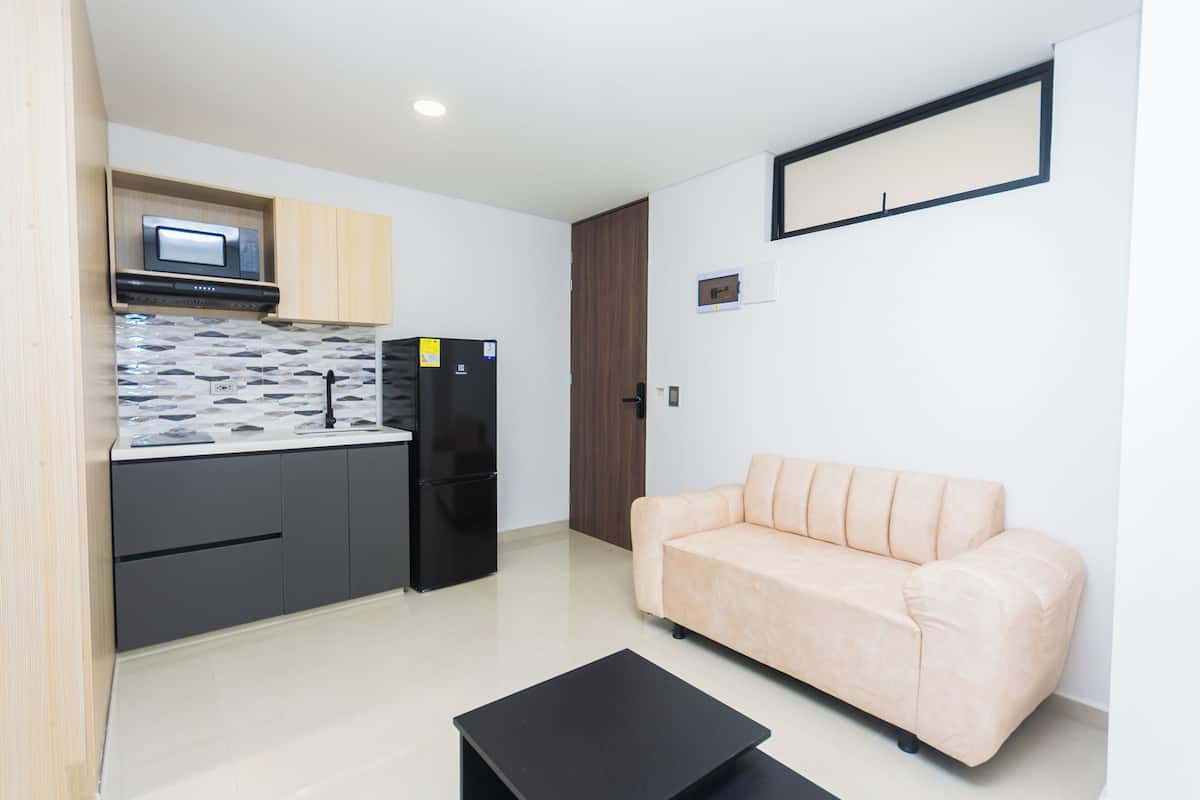 Una cocina moderna con microondas, refrigerador y salpicadero de azulejos. Hay un sofá beige y una mesa de centro negra en una sala de estar con un espejo grande en la pared.