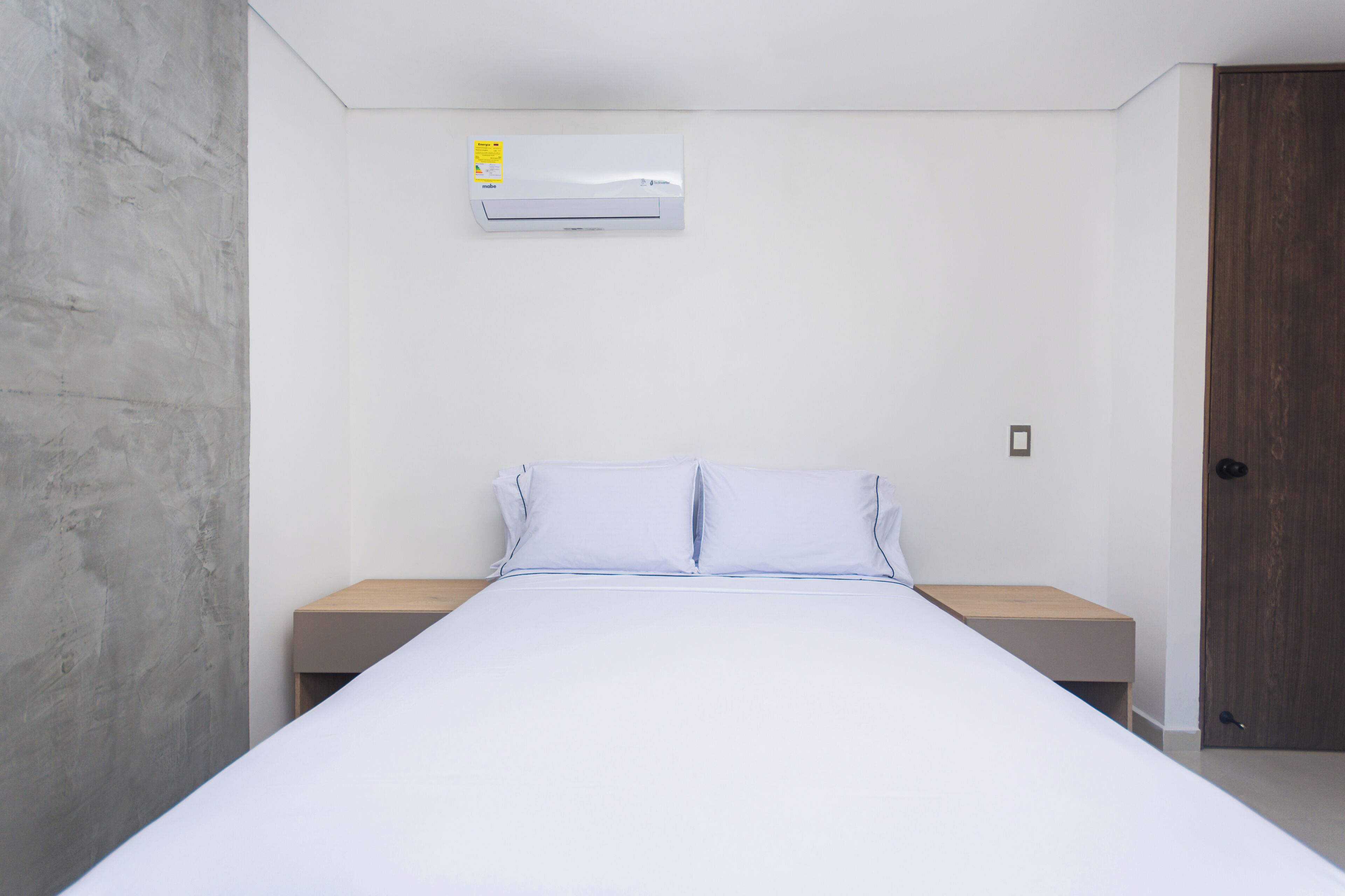 Une chambre à coucher comprenant un lit, deux tables de chevet, une porte en bois et un climatiseur fixé au mur.