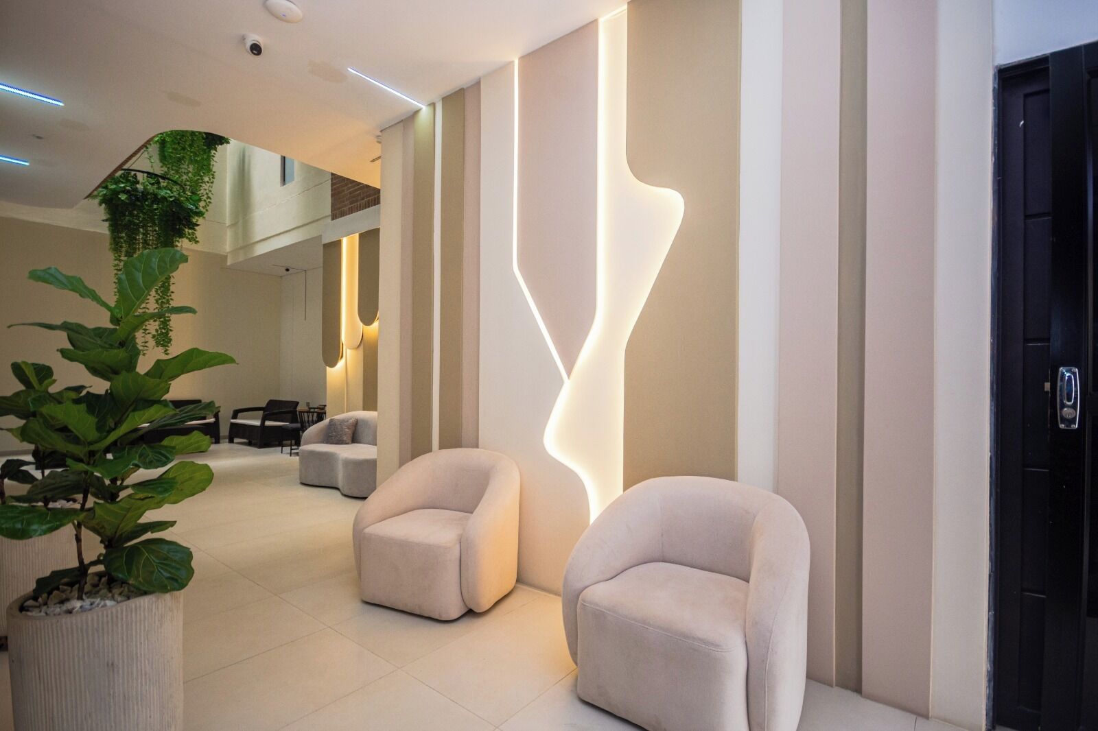 A modern lobby with a reception desk, two sofas, a potted plant, and a unique wall design.