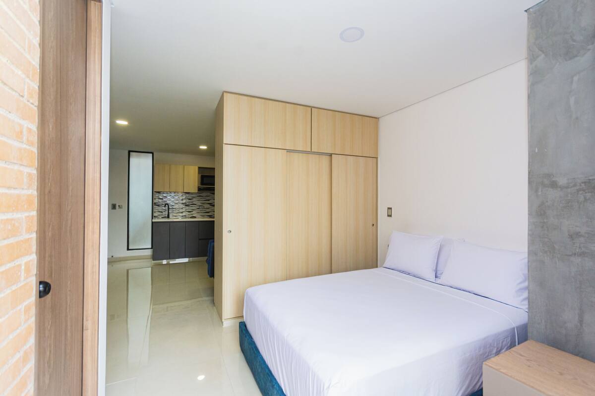 Un dormitorio con cama, armario y baño visible a través de una puerta abierta.
