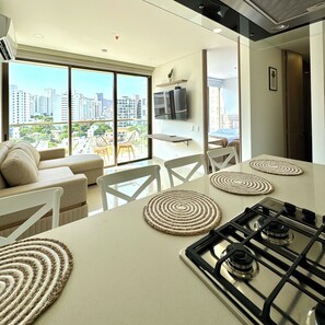 A modern kitchen with a large island, a dining area with white chairs, and a sofa. - Family Friendly 3BR Apt Plus Comfort and Amenities (Gaira)