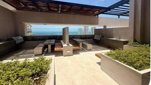 Un patio al aire libre con una parrilla, asientos y vistas al océano.