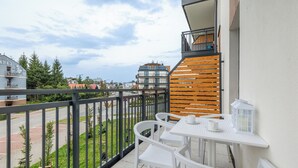 Een balkon met witte stoelen en een tafel, met uitzicht op een straat en groen.