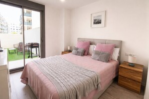 A bedroom with a bed, nightstands, a bedside table, a window with a view of buildings, and a door leading to a balcony. - Ap1142 in Denia With 1 Bedrooms and 1 Bathrooms (Denia)
