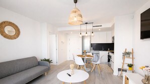 Uma sala de estar moderna com um sofá, uma mesa de jantar redonda e uma cozinha ao fundo.