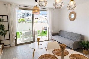 A modern living room with a grey sofa, a round dining table with woven placemats, and a large window with a view of a balcony and outdoor furniture. - Ap1142 in Denia With 1 Bedrooms and 1 Bathrooms (Denia)