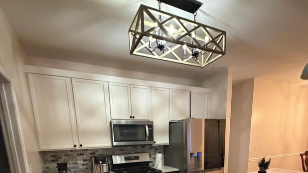 Cocina moderna con gabinetes blancos, electrodomésticos de acero inoxidable y una original lámpara colgante geométrica.