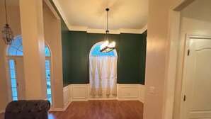 Una habitación amplia con pisos de madera, un candelabro y vistas a través de una ventana con cortinas.