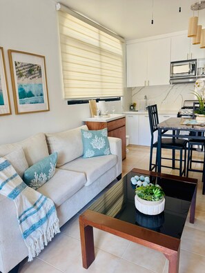 A modern living room with a sofa, coffee table, and kitchen area with cabinets and appliances. - Cozy 1-bedroom apartment with AC in soothing Sosúa (Sosúa)