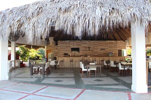 An outdoor bar area with a thatched roof, wooden bar counter, and multiple seating arrangements. - Cozy 1-bedroom apartment with AC in soothing Sosúa (Sosúa)