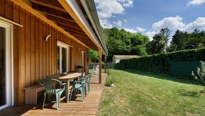 A wooden deck with a table and chairs, a covered patio area, and a grassy backyard. - Wooden Country Holiday Home with Private Terrace, Wi-Fi, and Air Conditioning (Corme-Royal)