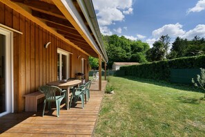 Une terrasse en bois avec une table et des chaises, un patio couvert et une cour arrière avec pelouse.
