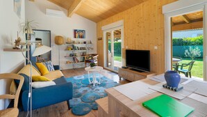 A modern living room with a wooden ceiling, a sofa, a television, and a bookshelf. - Wooden Country Holiday Home with Private Terrace, Wi-Fi, and Air Conditioning (Corme-Royal)