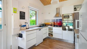 A modern kitchen with white cabinetry, a built-in microwave, and a large window. - Wooden Country Holiday Home with Private Terrace, Wi-Fi, and Air Conditioning (Corme-Royal)