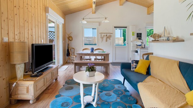 A cozy living room with a television, a dining area with a table and chairs, and a sofa. - Wooden Country Holiday Home with Private Terrace, Wi-Fi, and Air Conditioning (Corme-Royal)