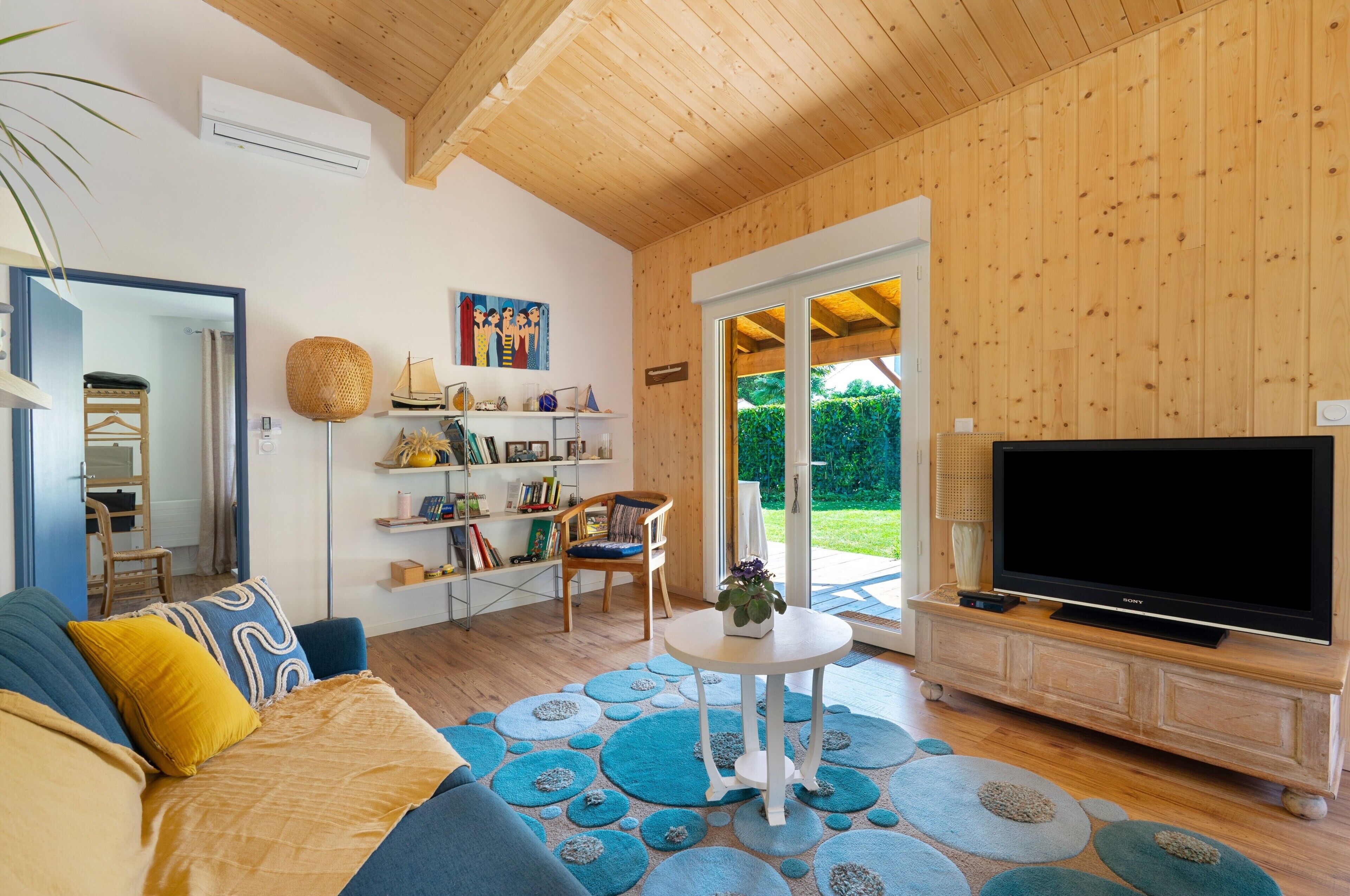 A modern living room with a wooden ceiling, a large flat-screen TV, a sofa, a coffee table, and a bookshelf.