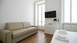 Minimalistiseen tyyliin sisustettu hotellihuone, jossa on sohva, televisio, lipasto ja sänky, ja sängyllä on pyyhkeet.