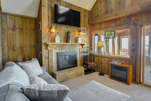 Een gezellige woonkamer met een open haard, een bank en een aan de muur bevestigde televisie.